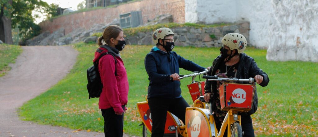 Turun linnan edustalla kaksi senioria kaupunkipyörien kanssa sekä fysioterapeutti neuvomassa.