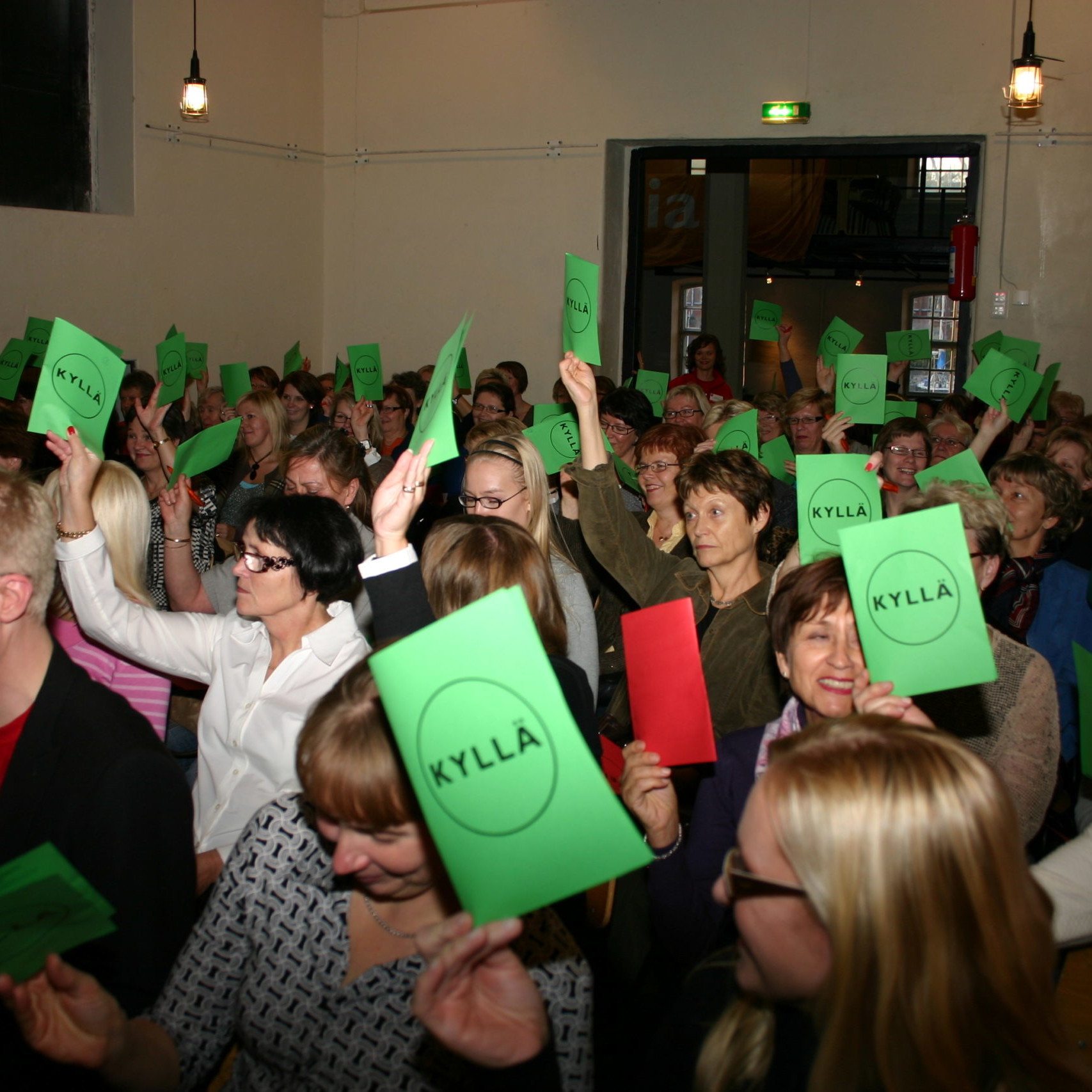 Yleisöä nostamassa vihreitä ja punaisia äänestyslippuja.