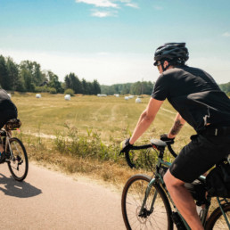 Kaksi pyöräretkeilijää pyöräilee aurinkoisessa maalaismaisemassa