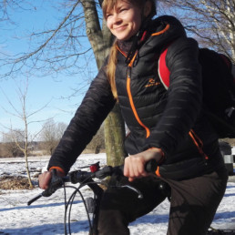 Pyöräilevä, hymyilevä nainen talvisessa maisemassa