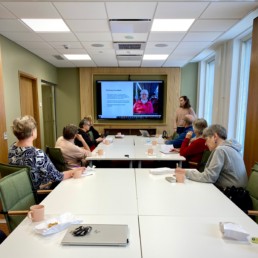 Ihmisiä kokoushuoneessa katsomassa presentaatiota screeniltä