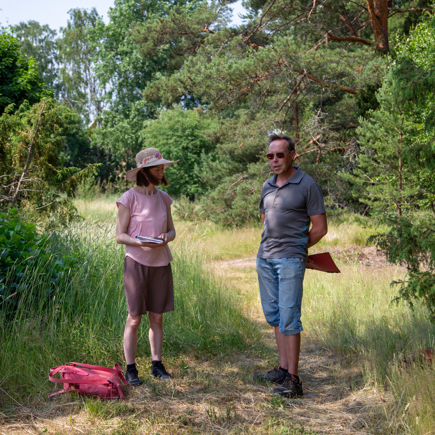 Kaksi henkilöä seisoo vierekkäin kedolla pensaiden keskellä