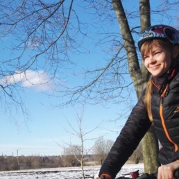 Pyöräilevä, hymyilevä nainen talvisessa maisemassa