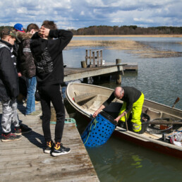 Ryhmä oppilaita laiturilla ja kalastaja veneessä laiturin edustalla