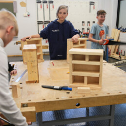 Kuva koulun teknisen työn luokasta, jossa neljä oppilasta rakentavat ötökkähotelleja