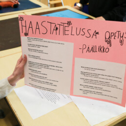 Oppilas pitää kädessä vaaleanpunaista julistetta otsikolla haastattelussa opetuspäällikkö