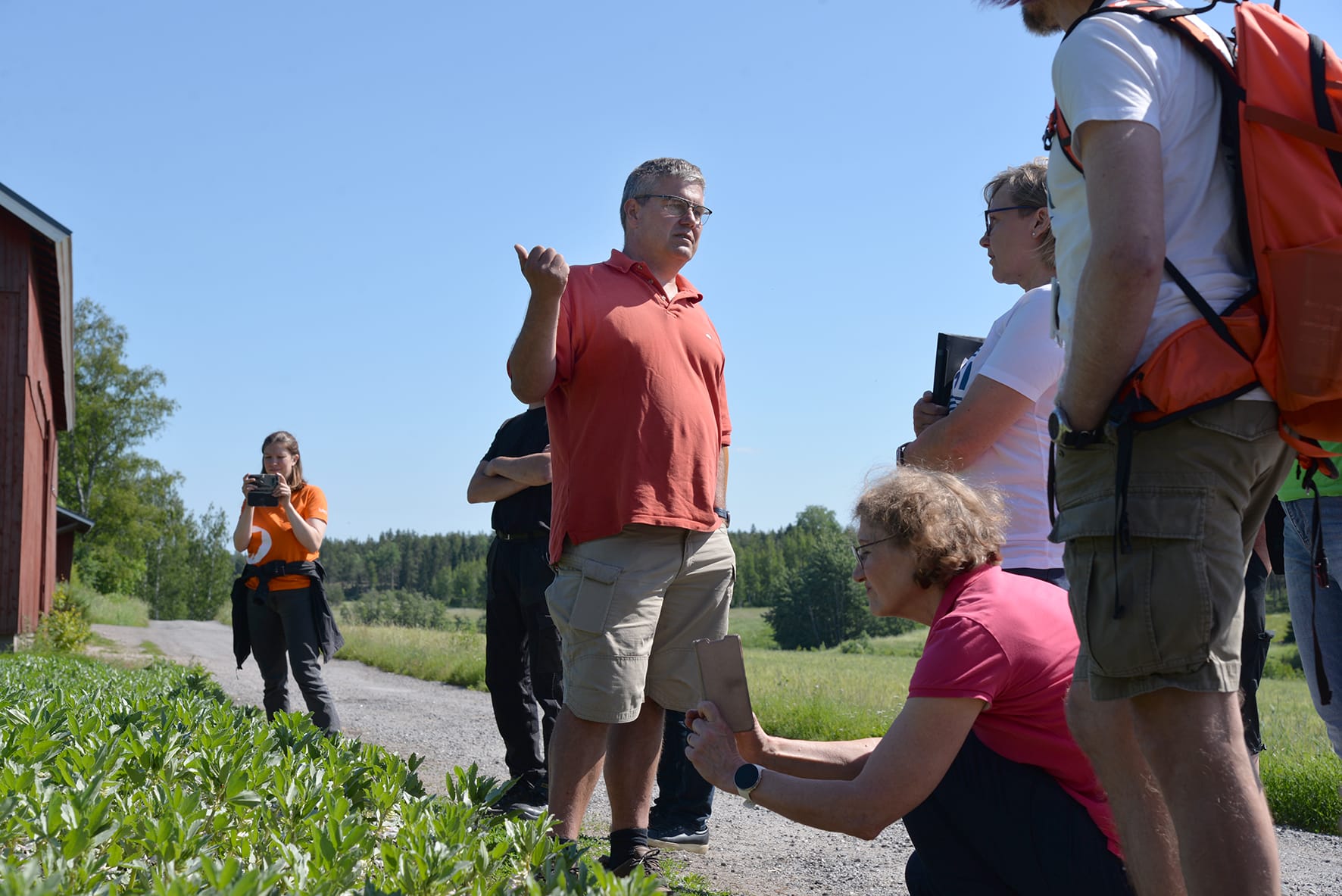 ryhmä ihmisiä pellon reunassa, henkilö ottaa valokuvia