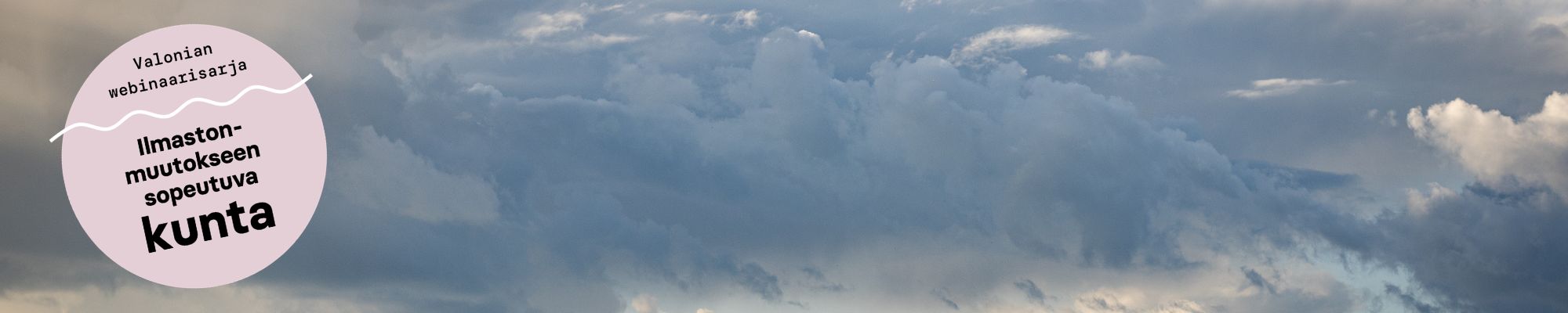 Panoraamakuva tummasta, sateisesta taivaasta. Oikeassa reunassa on vaaleanpunainen graafinen ympyrä, jossa lukee ’Valonian webinaarisarja – Ilmastonmuutokseen sopeutuva kunta’