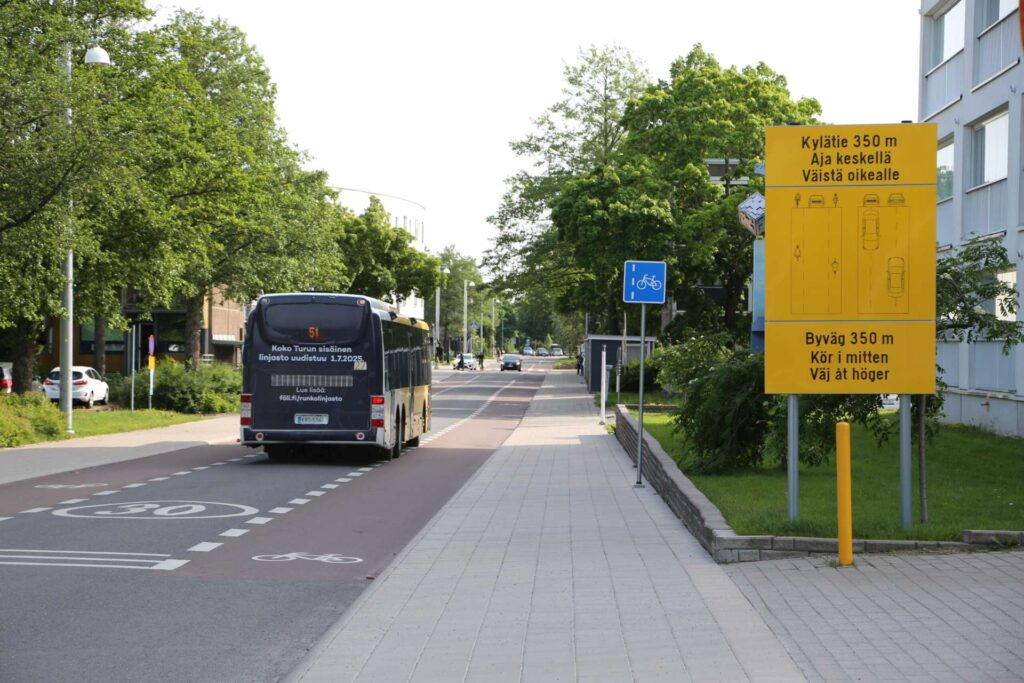 2-1-tie jonka varressa kävelytie ja linja-auto kulkee tietä takaapäin kuvattuna