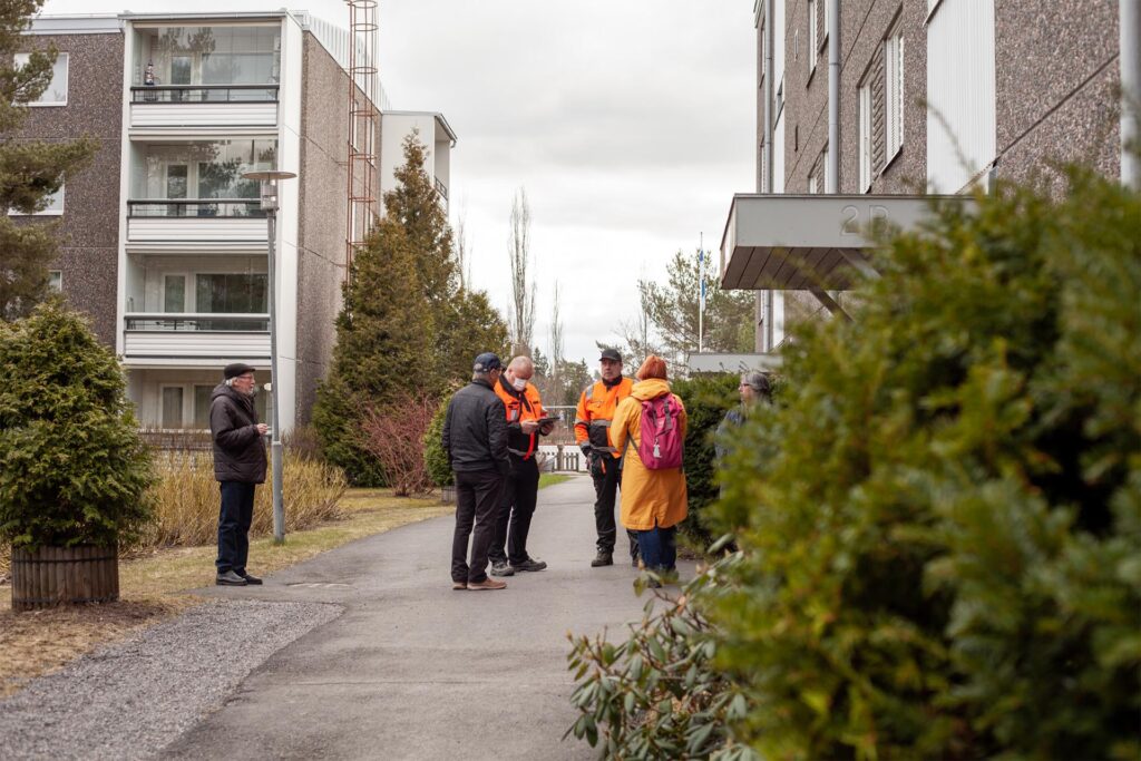 Kerrostalon piha, kuusi ihmistä seisoo ringissä puhumassa