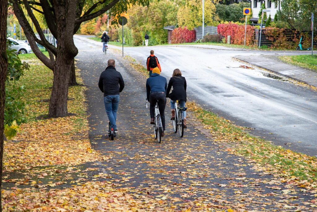 Syksyn lehtiä kadulla, kävelijöitä ja pyöräilijöitä katukuvassa.