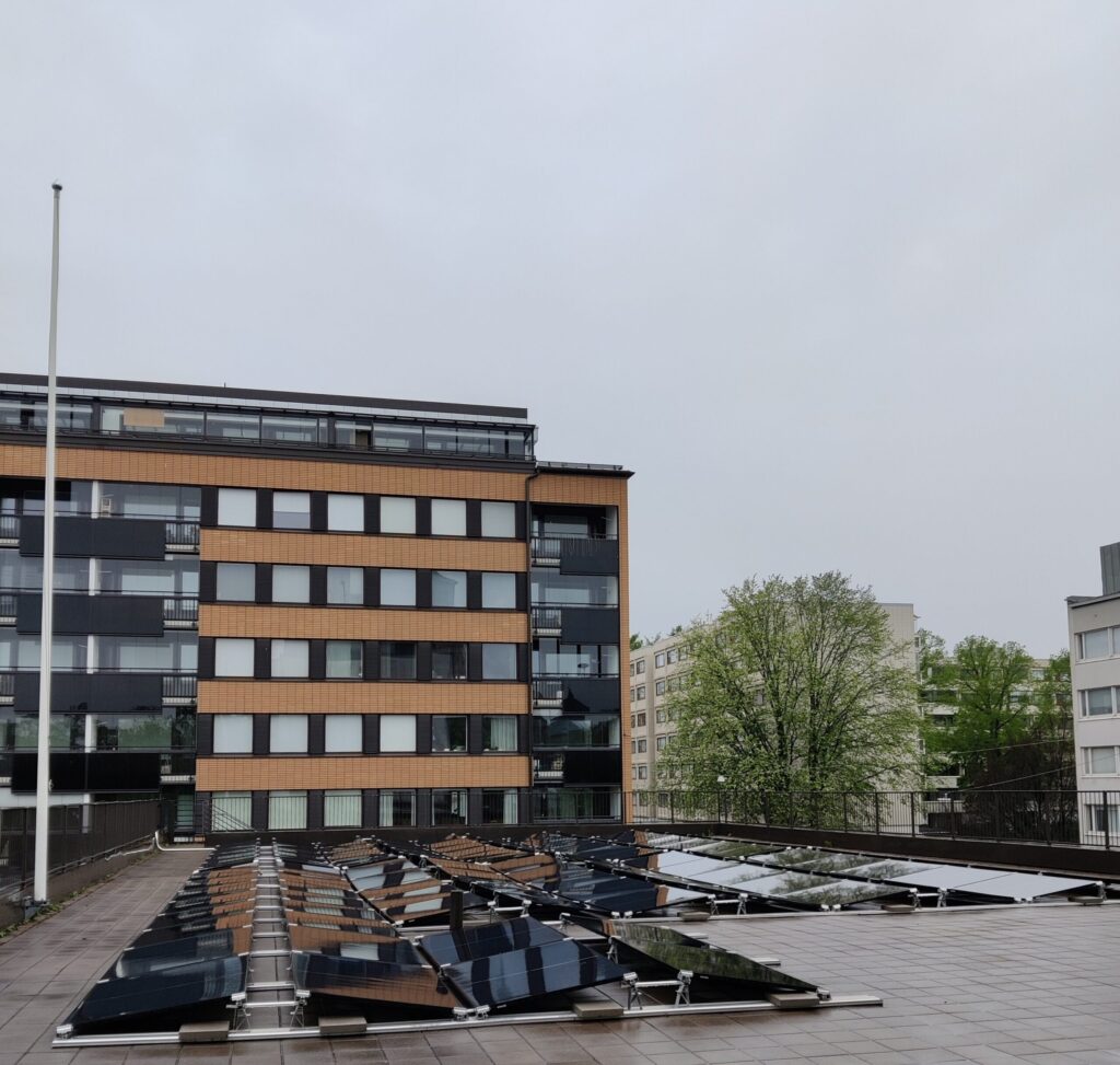 Kuva aurinkopaneeleista katolla. Taustalla kerrostaloja.