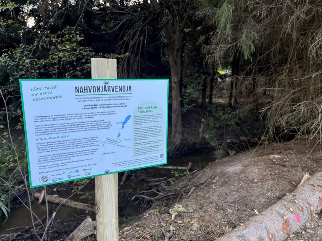 Vasemmassa reunassa infokyltti ja taustalla avautuu näkymä ojan pohjalle, jossa puusuisteita.
