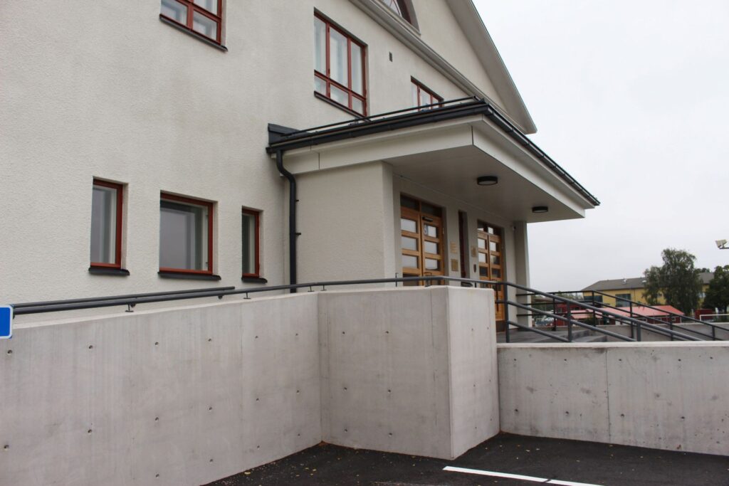 Valkoinen rapattu urheilutalo jonka edessä invaramppi