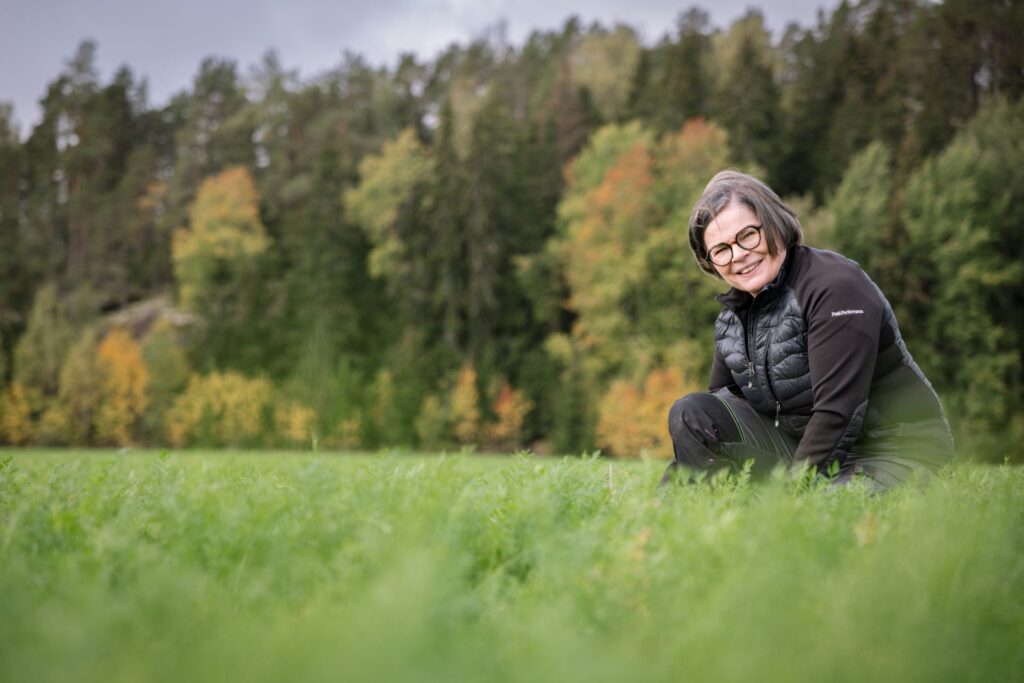 hymyilevä nainen kyykyssä pellolla