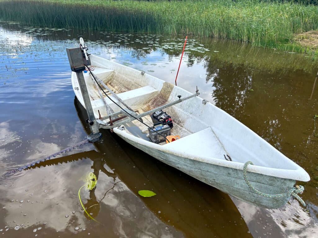 Vedessä vene, jonka kyljessä kiinni niittokone.