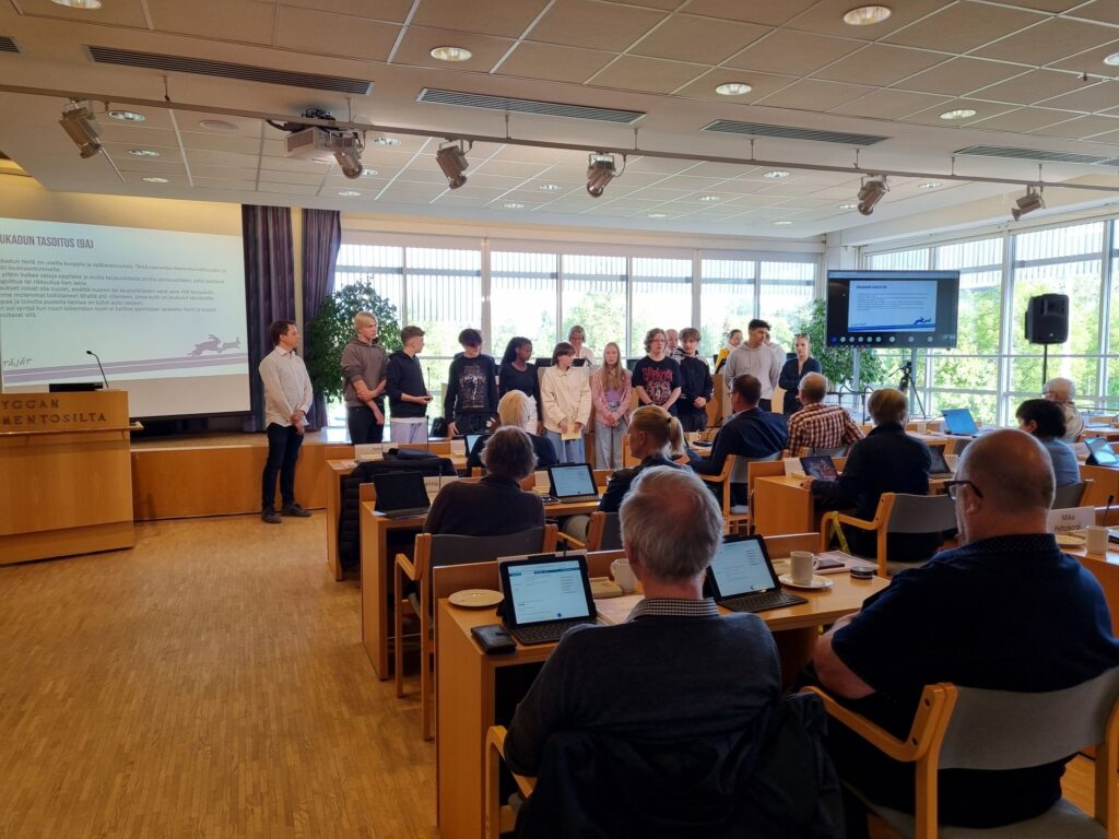 Ihmisiä istuu salissa kuuntelemassa puhetta