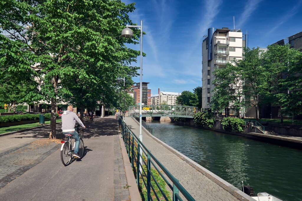 Pyöräilijä joen vieressä, taustalla kerrostalo