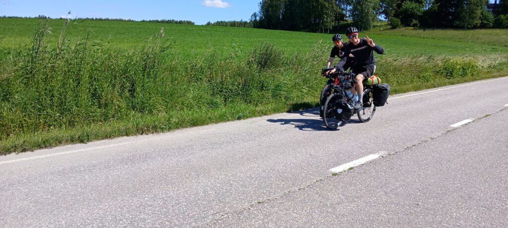 kaksi pyöräilijää maantiellä, taustalla peltoa