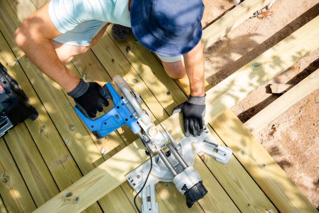 Henkilö rakentaa puuterassia ja sahaa lautaa jiirisahalla ylhäältä päin kuvattuna.