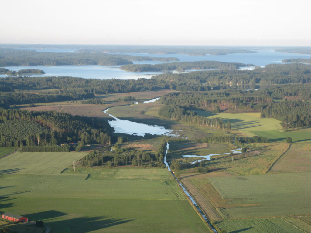 Ilmakuva Laukanlahdesta. Etualala näkyy peltoja, jota halkoo joki, joka laskee Laukalahteen. Taustalla metsää ja merta.