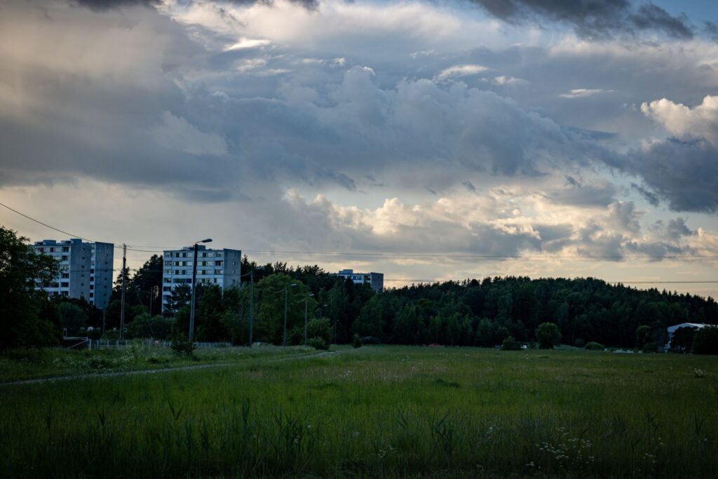 Panoraamakuva metsän reunassa olevista kerrostaloista tumman, sateisen taivaan alla.