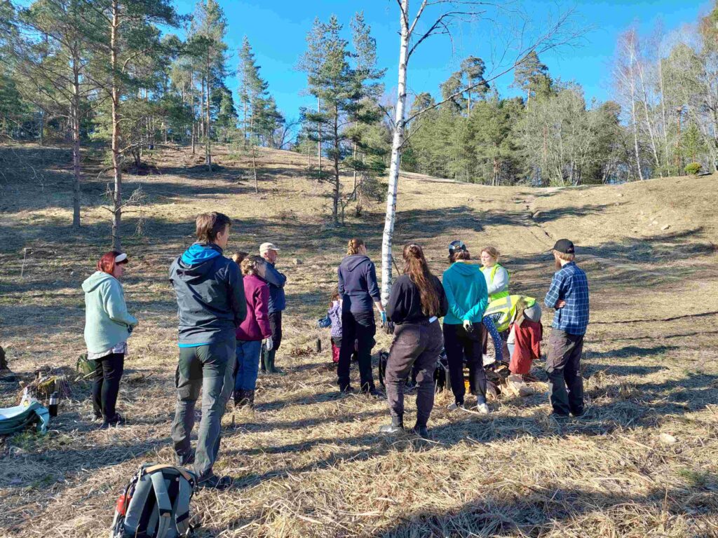 ihmisiä seisomassa ja katsomassa rinteeseen, puita, kevät