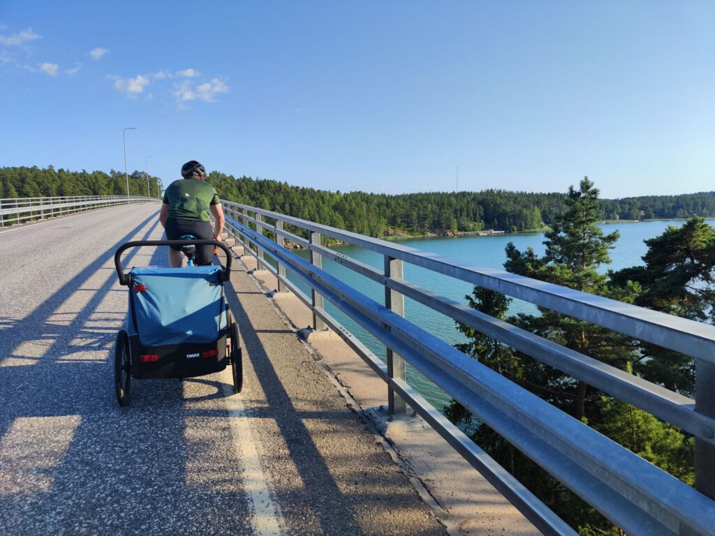 Mies pyöräilee sillalla meren rannalla ja vetää pyöräkärryä