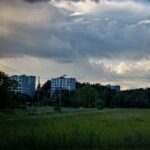 Panoraamakuva metsän reunassa olevista kerrostaloista tumman, sateisen taivaan alla.