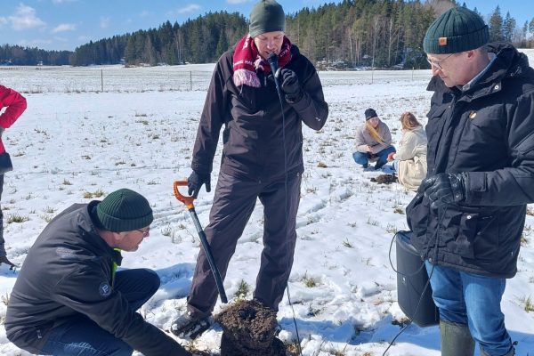 ihmisiä maahan kaivetun kuopan ympärillä tutkimassa maaperää