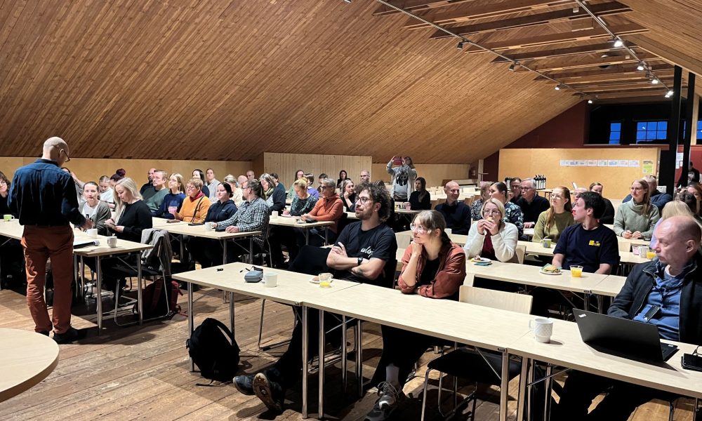 ihmisiä istumassa pöytien takana riveissä