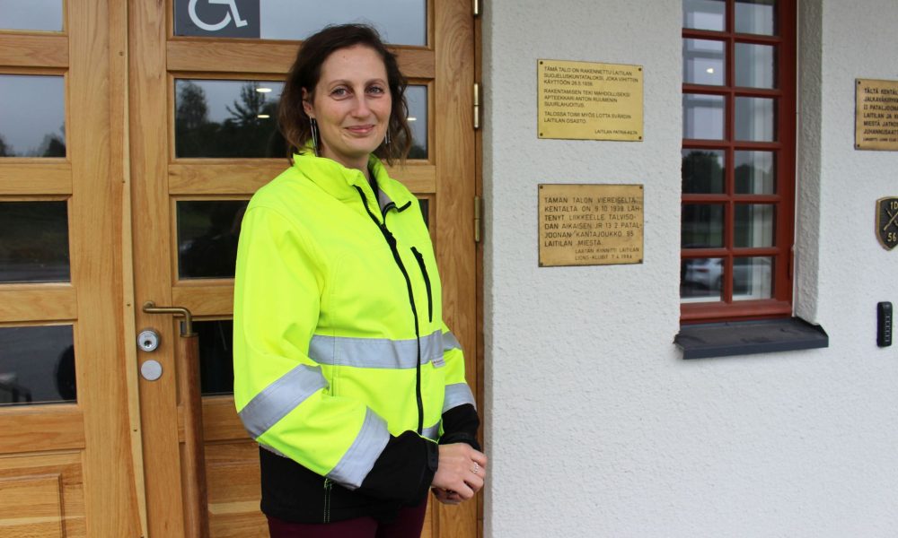 Puolikuva naisesta jolla on työmaatakki seisomassa ulko-oven edessä