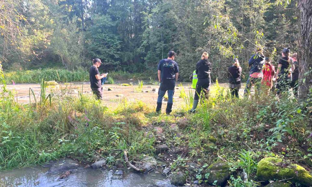 Ihmisiä kosken saarekkeella. Taustalla metsää.