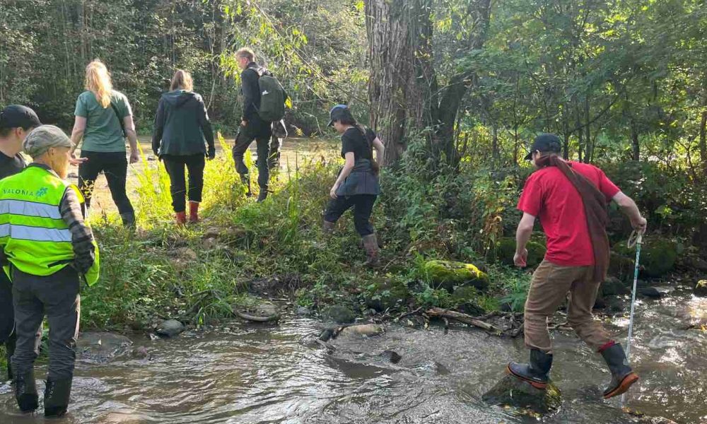 Henkilöitä uomassa, kosken reunalla ja hyppimässä uoman yli.